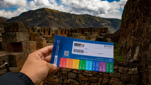 Boleto Turístico de Cusco (BTC) oficial de COSITUC en mano, con ruinas incas y los Andes de fondo