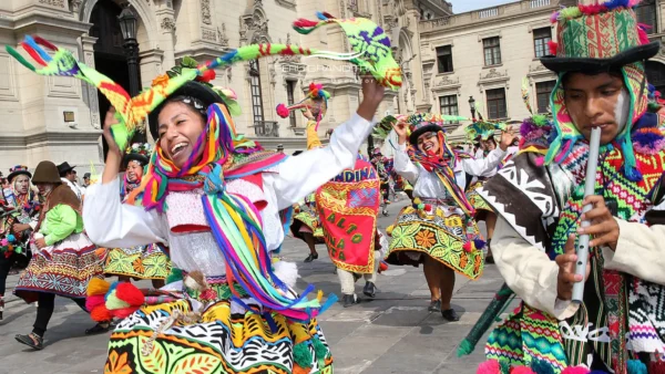 Danzantes de comparsa con trajes andinos coloridos durante el Carnaval de Ayacucho en Perú, interpretando danzas folclóricas en una plaza colonial histórica
