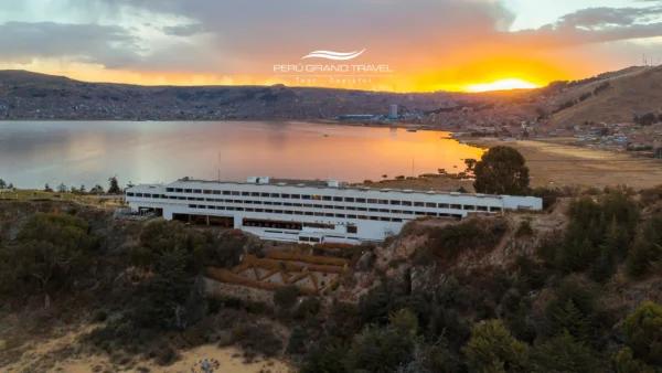 Hoteles de Lujo en Puno: vista panorámica al atardecer de un hotel frente al Lago Titicaca con la ciudad de Puno al fondo.