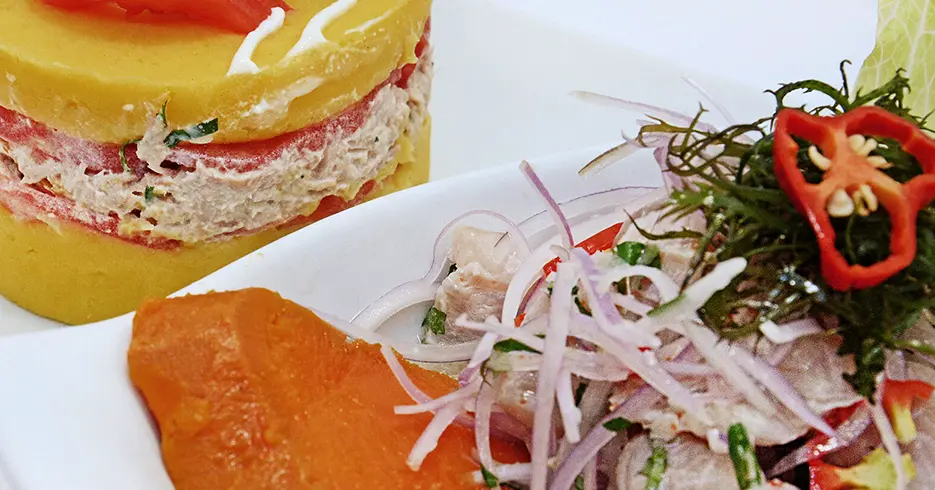 Los 12 Mejores Consejos para viajar a Perú 7 Consejos para viajar a Perú, Comida típica de Perú, ceviche y causa rellena, plato con cebolla, pescado, rocoto, camote y puré de papa con pollo y mayonesa