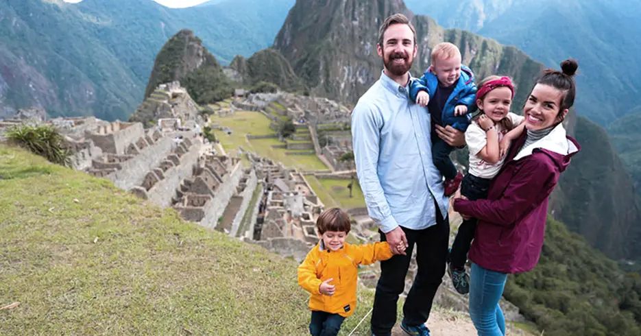 Perú en 10 días: Tu Guía a los mejores lugares 6 Familia feliz en Machu Picchu, 3 niños y dos adultos, todos sonriendo al fondo Machu Picchu, en la parte baja se ven los espacios arqueológicos y un ambiente lleno de color verde