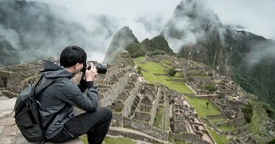 ¿Qué ropa llevar a Machu Picchu? La guía definitiva para viajeros 4 Turista fotografiando Machu Picchu, en la parte baja las construcciones incas y las montañas están cubiertas con niebla