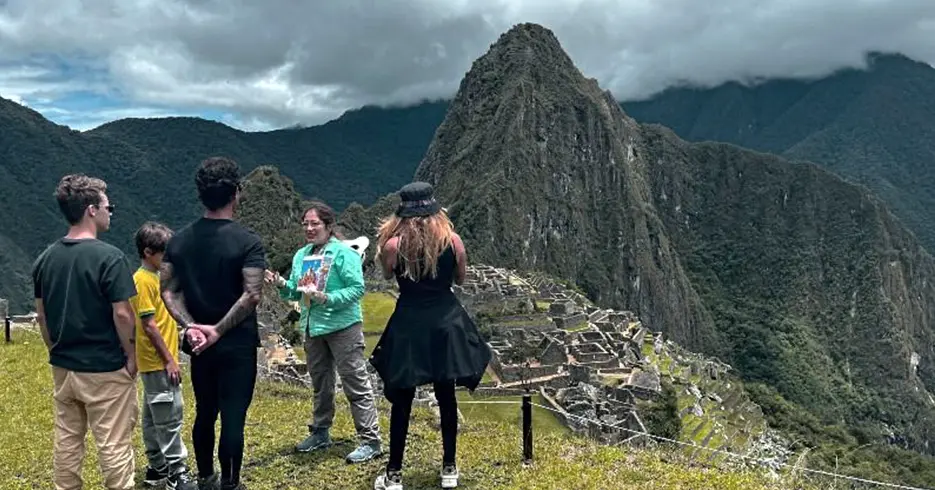 Guía de turismo explicando a los turistas sobre Machu Picchu, al fondo podemos observar los vestigios incas de la ciudadela y las montañas por todos lados
