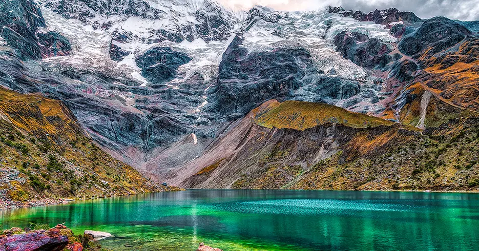 Viaje a los Andes en 11 días: Lugares impresionantes que debes conocer 6 Laguna humantay en un viaje a los Andes en cusco, agua turquesa, verde y azul cristalina, con el nevado humantay de fondo y montañas rocosas con pasto verde