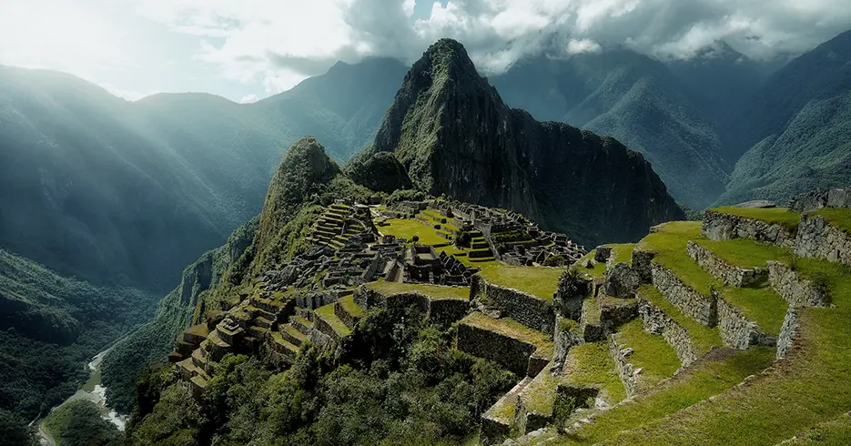 Machu Picchu con una vista bonita, con el sol iluminando la ciudadela inca y vista de los andenes y grandes montañas