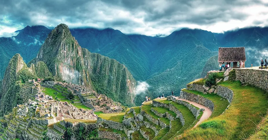 Machu Picchu de forma panorámica en una fotografía, la vista de la casa del almirante y los andenes de la ciudadela inca y en la parte baja a la izquierda se pueden observar las estructuras incas y las vistas de las montañas que rodean a Machu Picchu