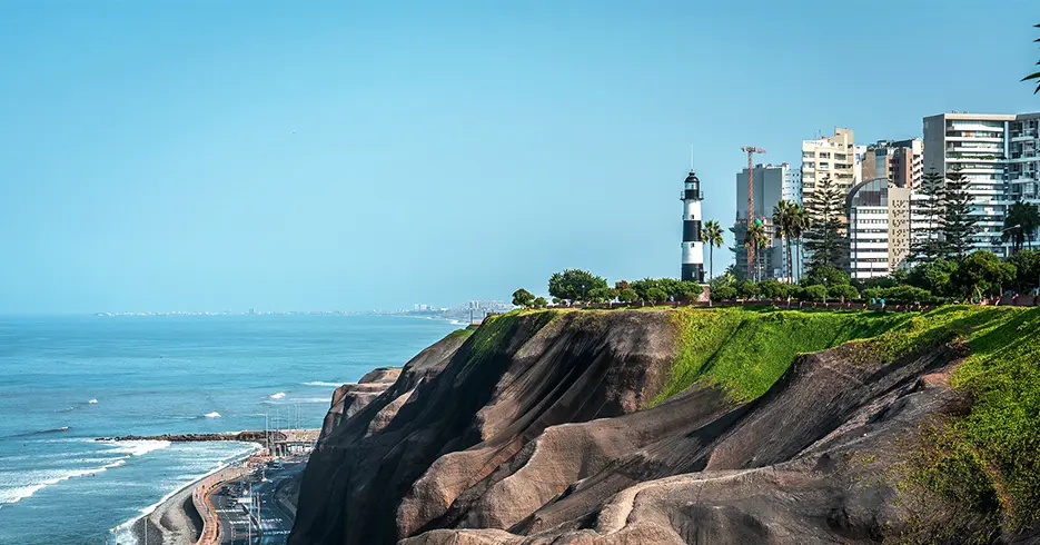 Qué Hacer en Perú 10 Días: Tu Guía definitiva a la Aventura 1 El malecón de Miraflores en la capital Lima, con vista al océano pacífico, un cielo despejado celeste con varios edificios y un faro.