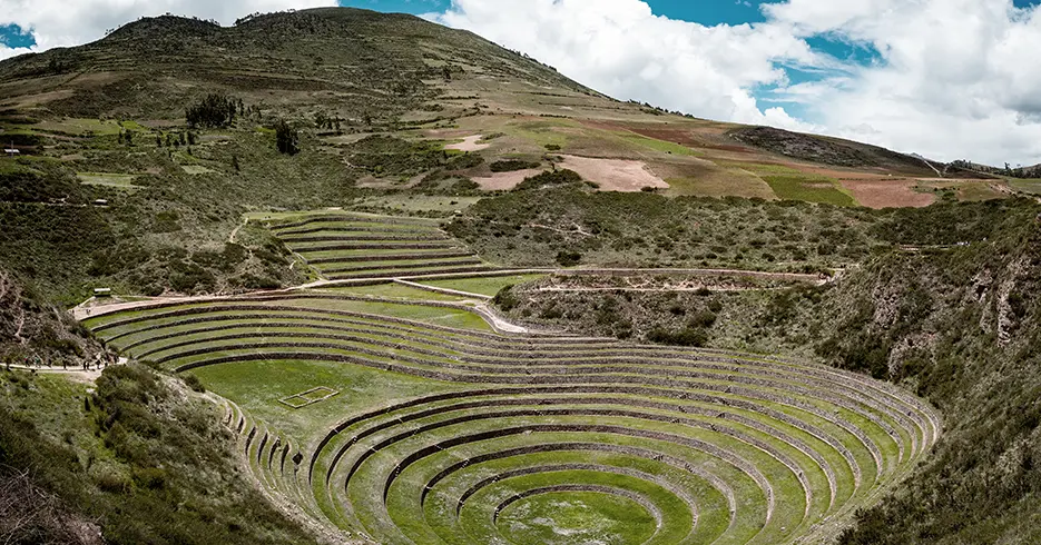 Cosas que hacer en Cusco: Lo mejor de la ciudad en un solo viaje 3 Cosas que hacer en cusco Vista de las terrazas circulares de Moray, un antiguo sitio Inca, rodeado de montañas y vegetación, con un cielo despejado.