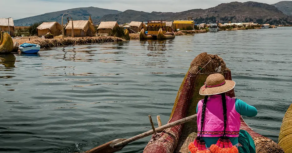 Mujer remando en un barco de totora en el lago Titicaca cerca de las islas flotantes de los uros