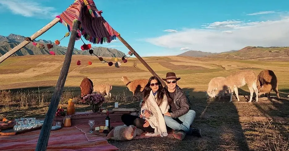 Pareja teniendo un pícnic en el valle sagrado con llamas alrededor con vistas increíbles del valle de cusco