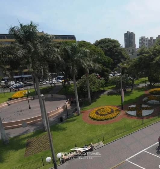 10 lugares para pasear en Lima que te harán amar de la ciudad 3 Vista do Parque Kennedy em Miraflores com jardins, visitantes e gatos descansando ao sol.