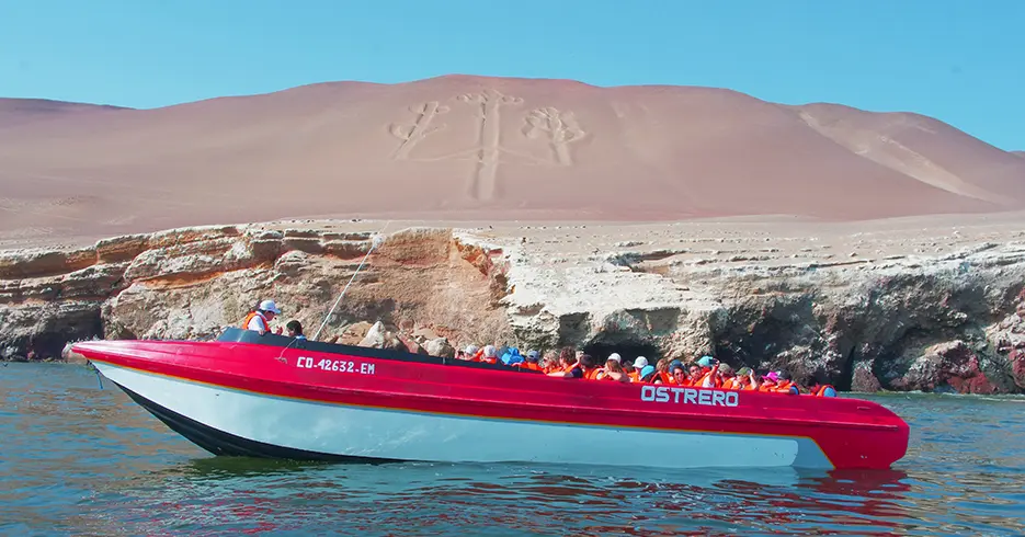 Qué Hacer en Paracas Perú: Experiencias que No Te Puedes Perder 6 Un barco con turistas y su guía en las islas ballestas, de fondo se ve el candelabro de paracas con dunas de arenas.