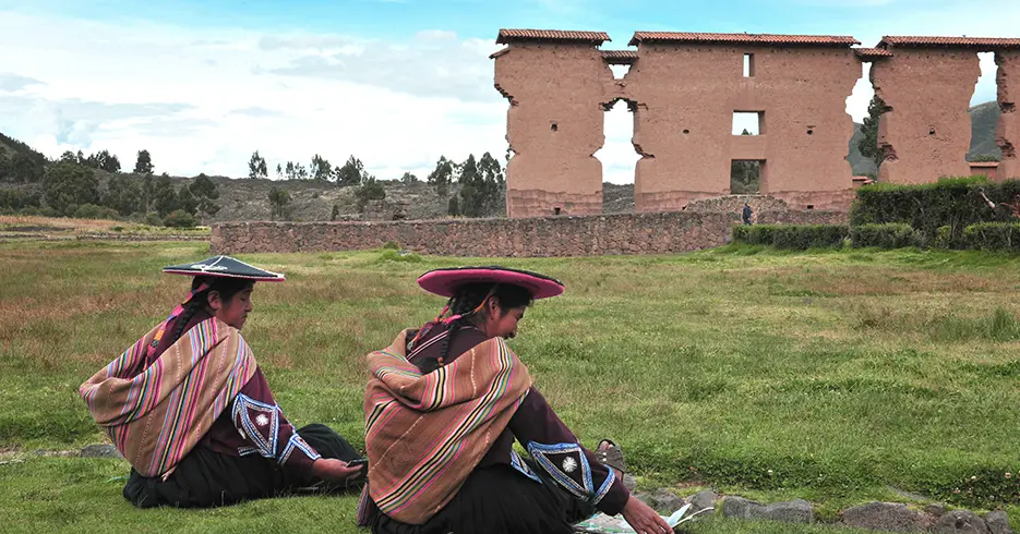 Perú en 10 días: Tu Guía a los mejores lugares 2 Mujeres locales en el centro arqueológico de Raqchi, sentadas en le pasto con sus sombreros y un cielo celeste despejado