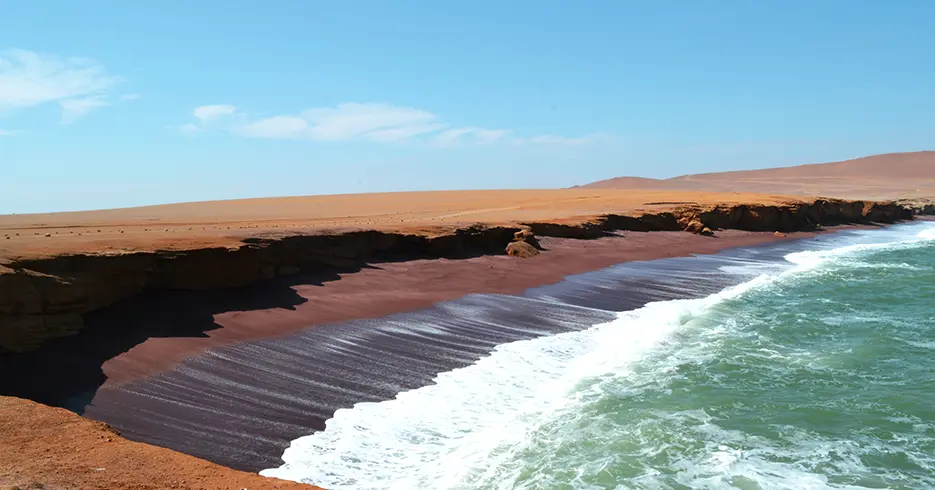 Qué Hacer en Paracas Perú: Experiencias que No Te Puedes Perder 4 La playa roja de paracas, con un paisaje lleno de arenas marrones y rojas, con un mar turquesa y pequeñas olas.