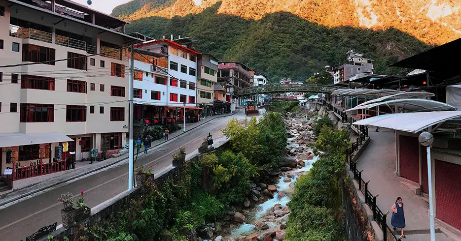 Pueblo de aguas calientes, paisaje lleno de casas y vegetación verde con un río lleno de piedras y un puente.