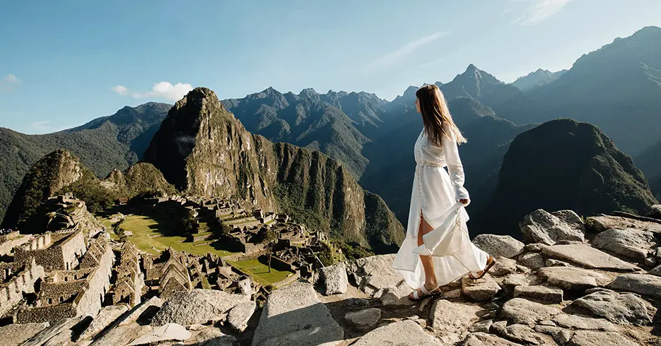 ¿Qué ropa llevar a Machu Picchu? La guía definitiva para viajeros 8 Qué ropa llevar a Machu Picchu, mujer con vestido blanco y viendo la ciudadela inca por un camino empedrado