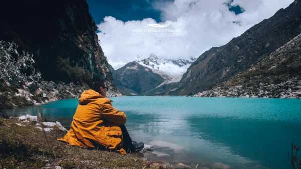 Viajero sentado en la cima de una montaña, contemplando las nubes y una laguna turquesa, ilustrando qué tan alto está Huaraz Perú a 3,052 metros.