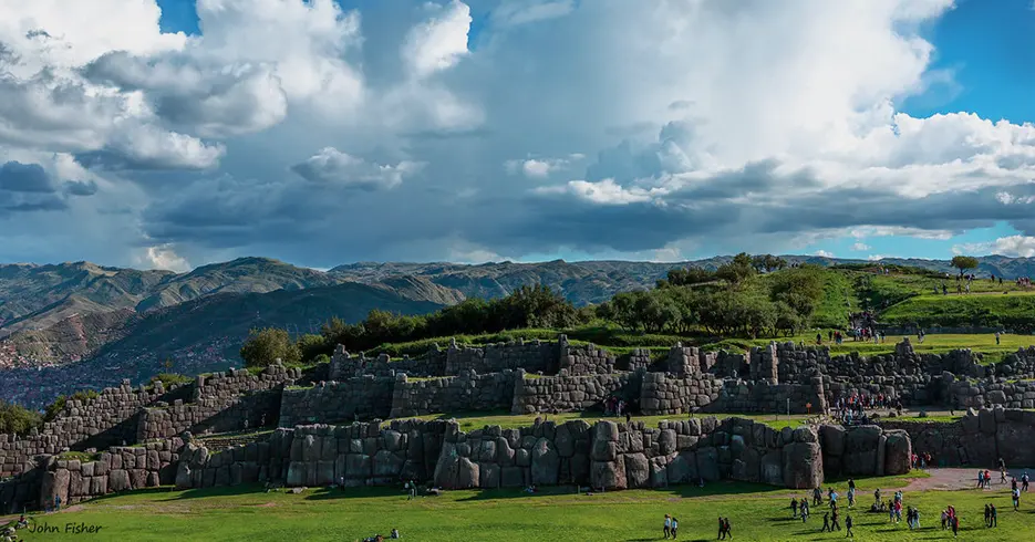 Haz Realidad Tu Viaje a Perú en 7 Días 2 Sitio arqueológico de sacsayhuaman con un cielo celeste y bastantes personas, con un paisaje verde y lleno de montañas el fondo