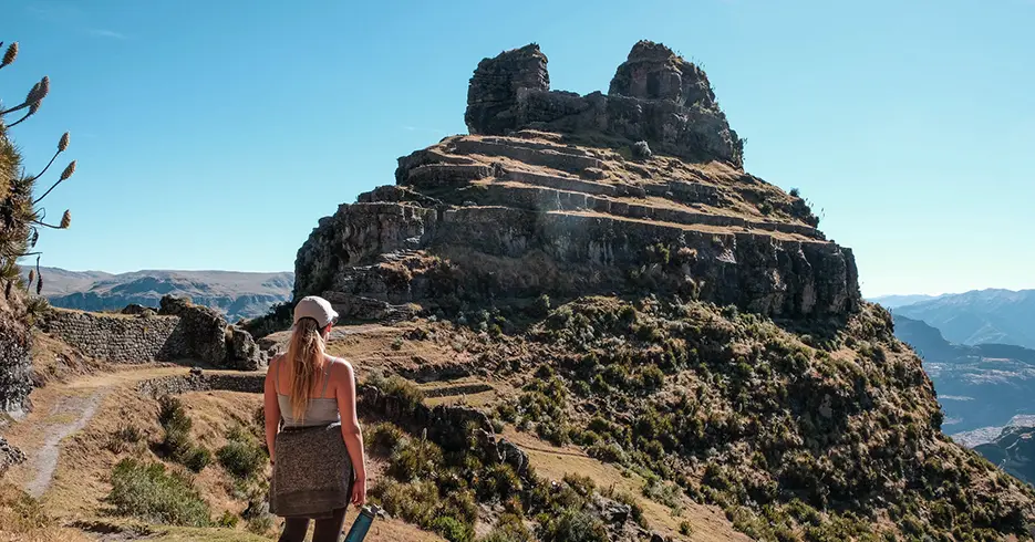 Los 10 Mejores Lugares Turísticos a Visitar en Cusco Perú 4 Mujer viendo la fortaleza de waqrapukara en cusco Perú, con un cielo celeste despejado y mucha vegetación alrededor de la fortaleza