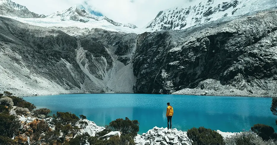 Turista en la laguna 69 con aguas azul claro y un nevado en la parte de arriba y algunos arbustos