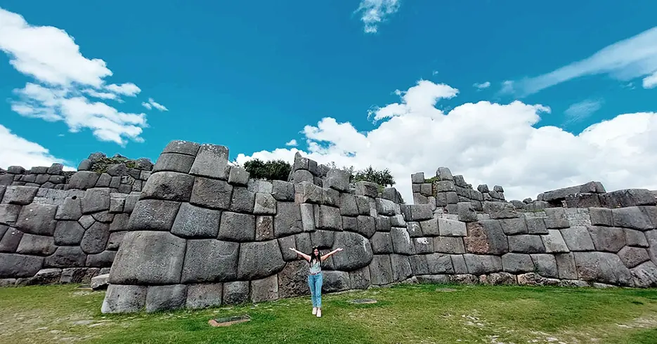¿Qué ropa llevar a Machu Picchu? La guía definitiva para viajeros 6 Turista en el centro arqueológico de Sacsayhuaman, con un cielo celeste y la vista de las grandes piedras de la fortaleza inca