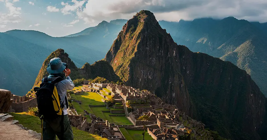 Haz Realidad Tu Viaje a Perú en 7 Días 4 Turista tomando fotos a Machu Picchu una de las 7 maravillas del mundo moderno, rodeada de montañas y abajo se ven los espacios incas.
