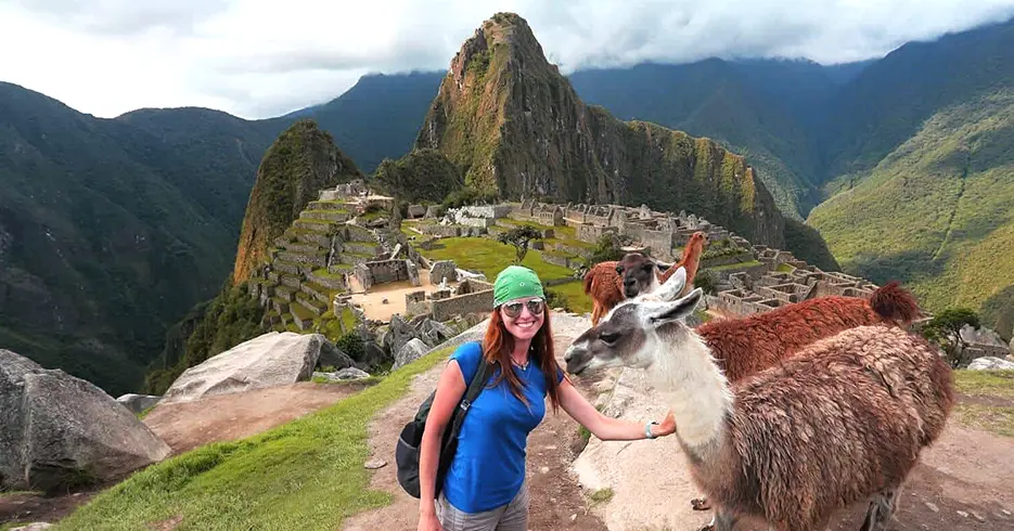 Turista posando con llamas con la vista de machu picchu al fondo
